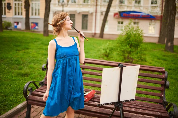 Bella ragazza-artista per strada in un abito blu, disegna sul cavalletto — Foto Stock