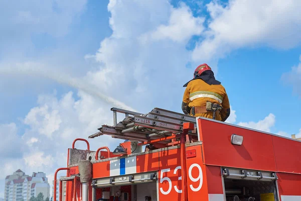 Bombeiro no telhado de um caminhão de bombeiros regando de uma mangueira de incêndio — Fotografia de Stock