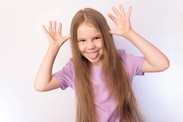 Cute little girl in a lavender shirt and with her hair, sticking his tongue out, making funny face, on a light background — Stock Photo, Image