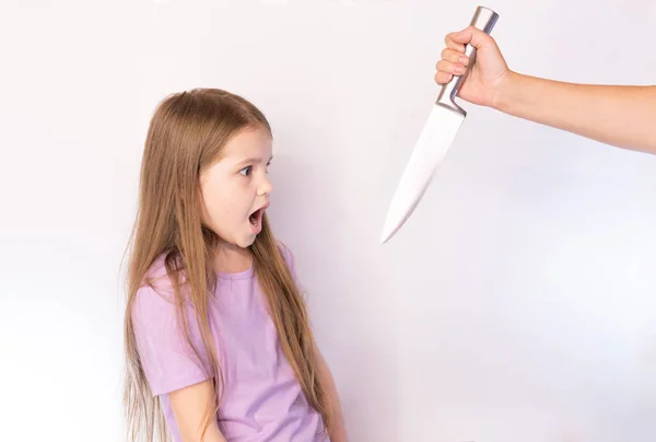 La niña, asustada mira el cuchillo que se balanceó sobre un fondo claro — Foto de Stock