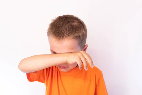 Cute little boy with tear-stained face and hand wipes his tears on a light background — Stock Photo, Image