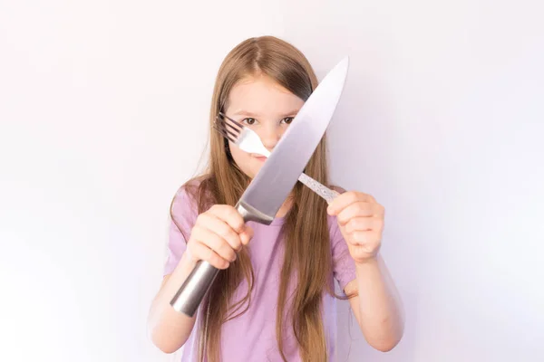 Mała śliczna dziewczyna trzyma nóż i widelec poprzek na jasnym tle — Zdjęcie stockowe