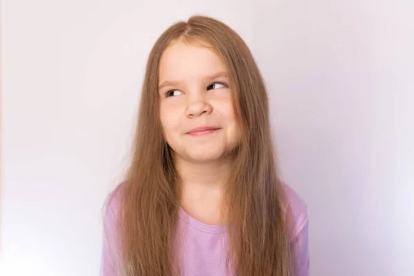 Piccola ragazza carina rotola gli occhi, con i capelli, sorridendo furbescamente su uno sfondo leggero — Foto Stock