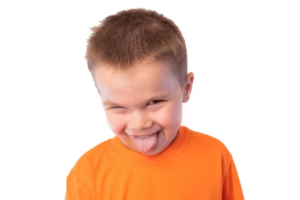 Süße kleine Junge streckt seine Zunge aus und lächelt, beobachtet, wie sie ihren Kopf neigt und ein Auge vor einem hellen Hintergrund schließt — Stockfoto