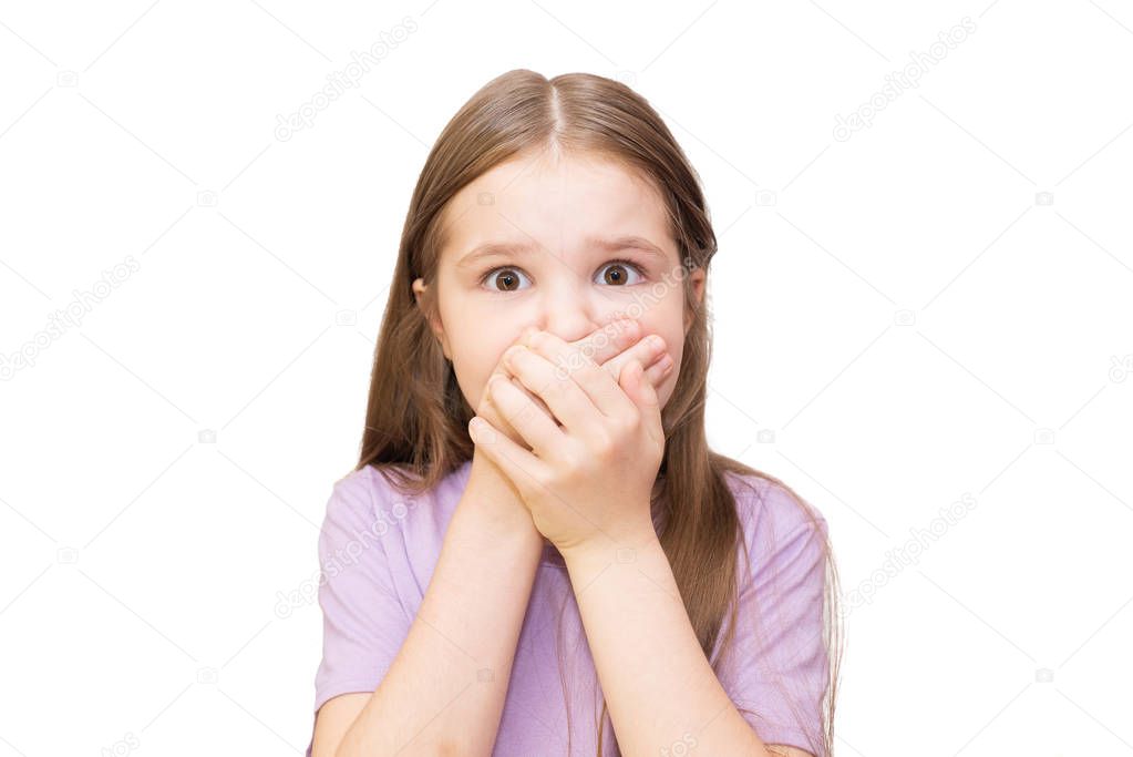 The little girl closes a mouth hands with widely opened eyes. It is isolated on a white background.