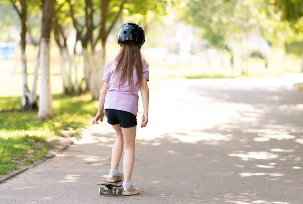 小さな女の子が後ろからスケートボードに乗っている. — ストック写真