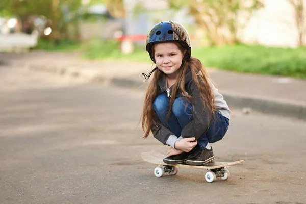 Ein kleines Mädchen hockt auf einem Skateboard. — Stockfoto