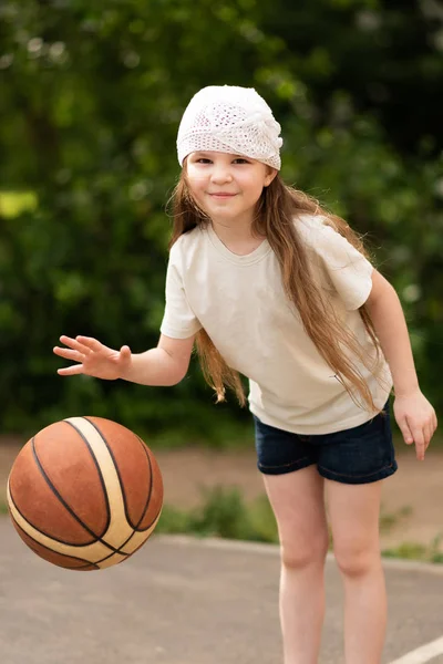 Μικρό κορίτσι με μακριά μαλλιά με μια μπάλα του μπάσκετ στα χέρια της — Φωτογραφία Αρχείου