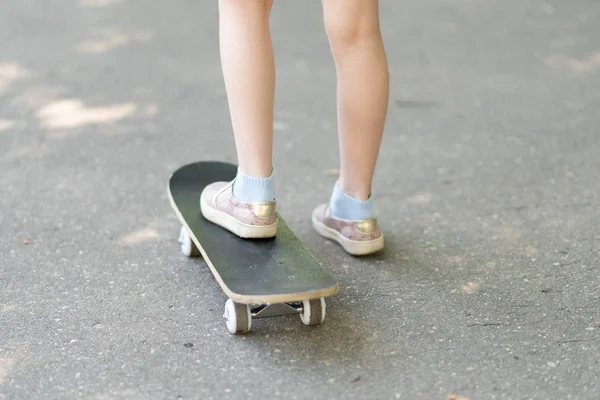 Benen van een klein meisje op een skateboard. — Stockfoto