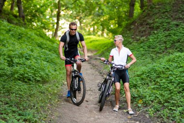 Bisikletli bir adam ve bir kadın tepeden aşağı iner..