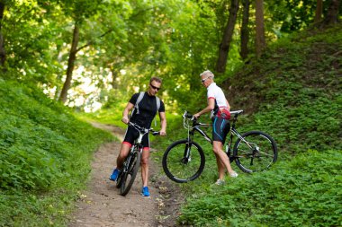 Bisikletli bir adam ve bir kadın tepeden aşağı iner..