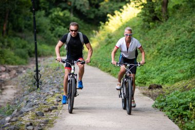 Bisikletli bir adam ve bir kadın parkta bir yol boyunca binmek.