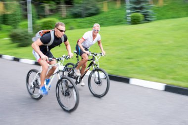 Bir adam ve bir kadın bir parkta bir yol boyunca bisiklet ebinmek, odak dışında.