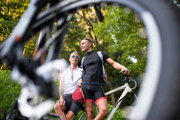 Güzel adam ve kadın bir bisiklet tekerleği ile, bir bisiklet yanında durmak.