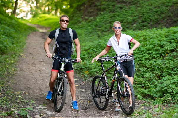 Bir parkta bir sokakta bisiklet üzerinde gülümseyen adam ve kadın.