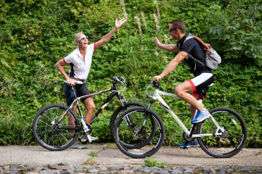 Bisikletli bir adam ve bir kadın sokakta birbirlerine el sallıyorlar..