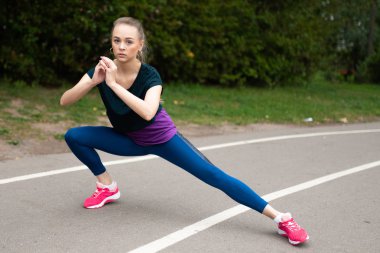 Atletik kız bir sokak koşu bandı üzerinde germe yapıyor.