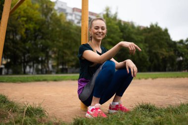 Atletik sarışın kız futbol gol kale direğine yakın oturuyor.