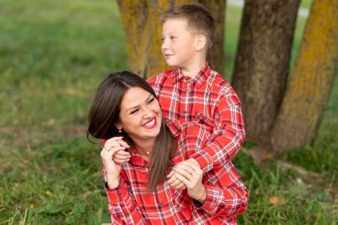 Annesi neşeyle gülüyor, oğlunu kollarından tutuyor, o da onu sırtından kucaklıyor..