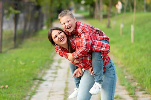 Mom, laughing, holds on his back a laughing son.