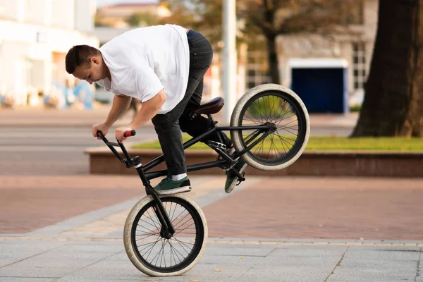 El tipo en la bicicleta BMX realiza un truco en la rueda delantera . —  Fotos de Stock
