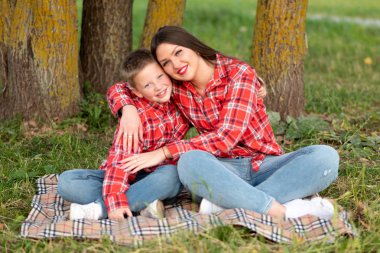 Anne ve oğlu, lotus pozisyonunda yatak örtüsünde oturup sarılıyorlar..