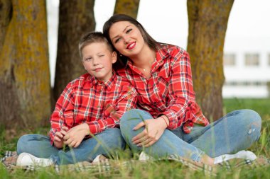 Anne ve oğlu, lotus pozisyonunda yatak örtüsünde oturup sarılıyorlar..