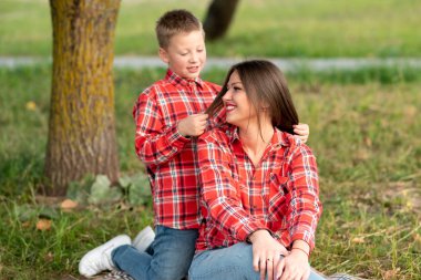 Oğlu, annesinin arkasında diz çökmüş, saçlarıyla oynuyor..