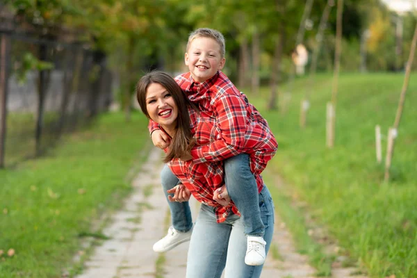 Mom, laughing, holds on his back a laughing son.