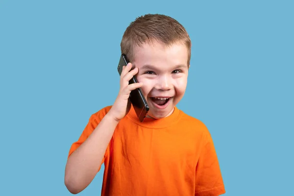 Το αγοράκι μιλάει στο τηλέφωνο και εκφράζει έκπληξη. Απομονωμένα σε μπλε φόντο. — Φωτογραφία Αρχείου