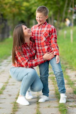 Anne ve oğlu parkta yürürken mutlu bir şekilde gülümsüyor..