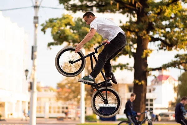 The guy performs a stunt on BMX, jumping high up, and touches the front wheel.