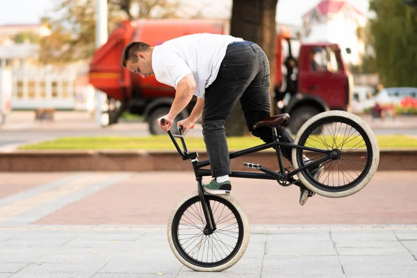 Un joven en una bicicleta BMX, monta en la rueda delantera, frenando con el pie . —  Fotos de Stock