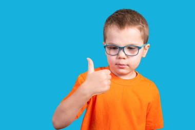 Gözlüklü küçük çocuk başparmağını kaldırdı. Mavi bir arkaplanda izole edilmiş.