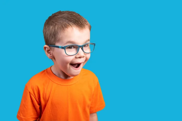 Il bambino con gli occhiali è molto sorpreso. Isolato su sfondo blu . — Foto Stock