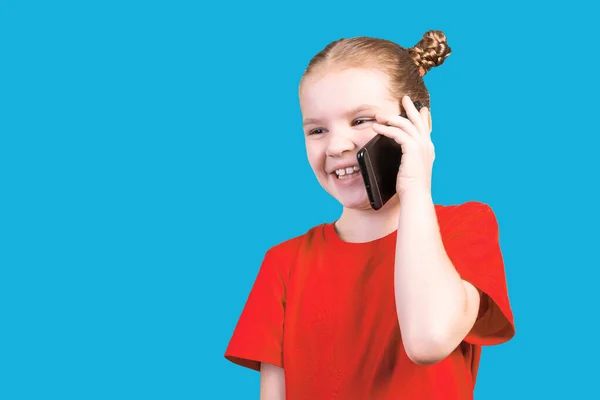Kleines nettes Mädchen, im hellen T-Shirt, mit Smartphone im Gespräch und lachend, isoliert auf blauem Hintergrund. — Stockfoto