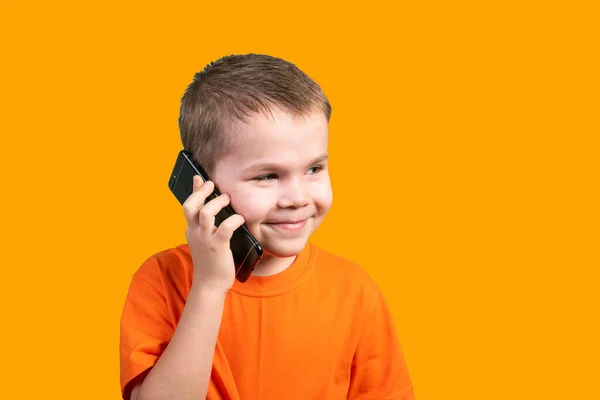 Kleine jongen is aan de telefoon. Geïsoleerd op een oranje achtergrond. — Stockfoto