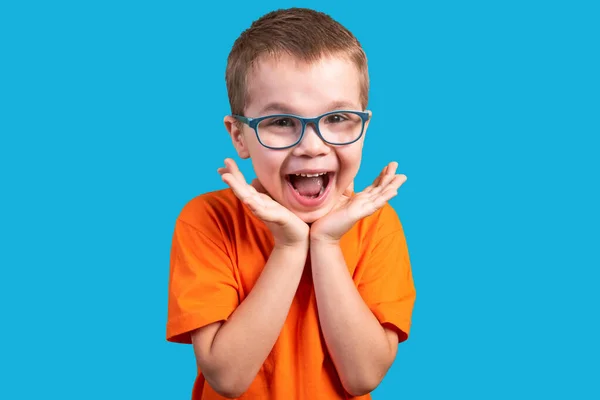 Der kleine Junge mit der Brille ist sehr überrascht. isoliert auf blauem Hintergrund. — Stockfoto