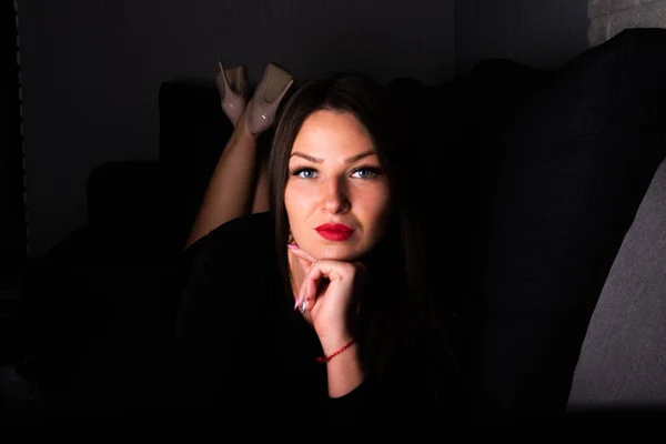 Vacker flicka i svart klänning ligger på en soffa. — Stockfoto