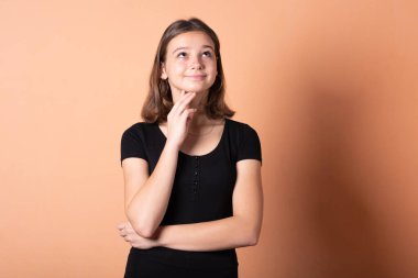 Kız düşündü ve elini ağzına koydu, açık turuncu arka planda..