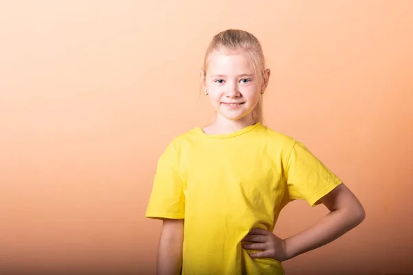 Dívka si položila ruce na boky, na světle oranžové pozadí. — Stock fotografie