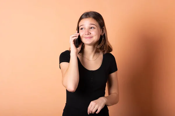 A menina está falando ao telefone de surpresa, em um fundo laranja claro . — Fotografia de Stock