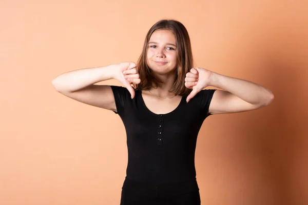 Ragazza mostra un dito verso il basso, su uno sfondo arancione chiaro . — Foto Stock