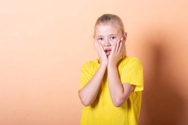 Güzel küçük kız açık turuncu bir arka planda utanıyor..