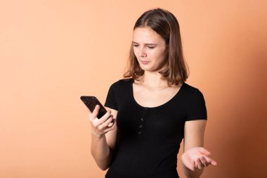 Açık turuncu arka planda akıllı bir telefonla hoşnutsuzluk gösteren bir kız..