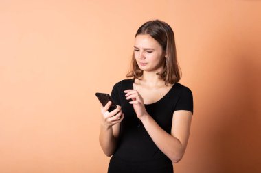 Açık turuncu arka planda akıllı bir telefonla hoşnutsuzluk gösteren bir kız..