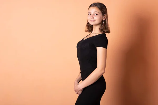 Una chica en un vestido negro, sobre un fondo naranja claro . —  Fotos de Stock