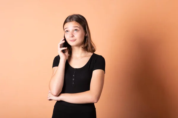 A menina está falando ao telefone de surpresa, em um fundo laranja claro . — Fotografia de Stock