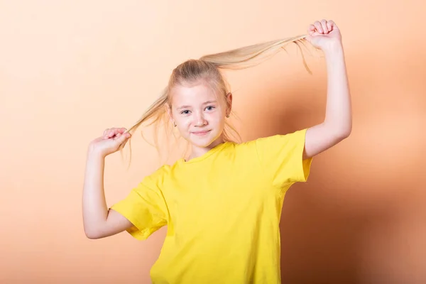 Ein Mädchen zieht sich an den Haaren auf hellorangefarbenem Hintergrund. — Stockfoto