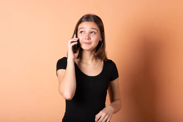 A menina está falando ao telefone de surpresa, em um fundo laranja claro . — Fotografia de Stock